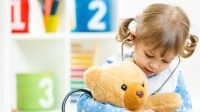 Cute kid girl playing doctor with plush toy at home